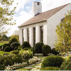 a small white house surrounded by trees and bushes in front of it is an attractive garden