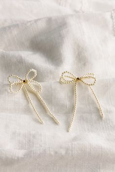 The Tarah Cream Pearl Bow Dangle Earrings, where timeless elegance meets modern sophistication. Crafted with meticulous attention to detail, these earrings exude charm and grace, perfect for any occasion. Each earring boasts delicate mini cream pearls, evoking a sense of refined beauty. A single shimmering gold pearl detail adds a touch of opulence, creating a captivating contrast against the creamy backdrop. The charming earring bow-shaped design, a symbol of femininity and grace. Whether paire Cream Pearl Drop Jewelry, Cream Pearl Drop Earrings For Formal Occasions, White Pearl Charm Earrings For Party, Cream Pearl Earrings For Formal Occasions, Chic Cream Jewelry For Formal Occasions, Chic Cream Jewelry For Formal Events, Chic Cream Formal Jewelry, White Pearl Chain Earrings For Evening, Delicate White Earrings With Pearl Chain