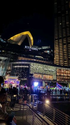 people are standing outside at night in front of a large building with lights on it