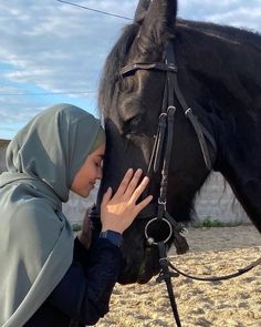 a woman in a hijab petting a black horse's head on the beach