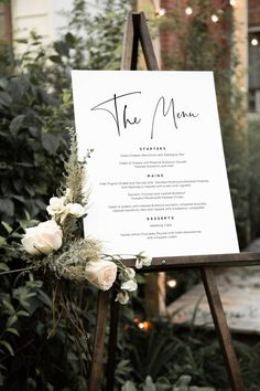 a welcome sign with flowers on it in front of some bushes and greenery at an outdoor venue