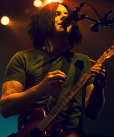 a man with long hair playing a guitar in front of a microphone and some lights