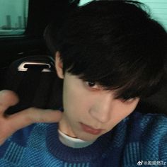 a young man with black hair wearing a blue sweater and looking at the camera while sitting in a car