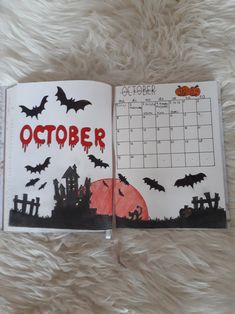 an open calendar with bats on it and the word october written in red ink, sitting on a fluffy white surface