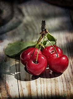 three cherries sitting on top of a wooden table next to a green leaf,