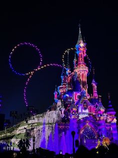 the disneyland castle is lit up at night with colorful lights and decorations on it's side