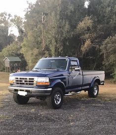 a blue pick up truck parked in a parking lot next to some trees and bushes