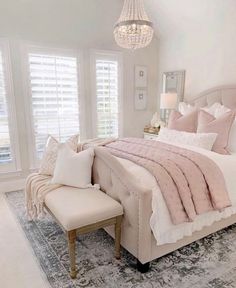 a bedroom with a large bed, chandelier and two windows that have white shutters