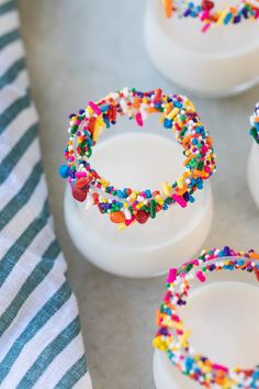 colorful sprinkles are on the rim of white cups with candy in them