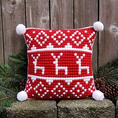 a red and white pillow sitting on top of a brick wall next to pine cones