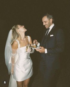 a man in a tuxedo and a woman in a white dress are laughing at each other