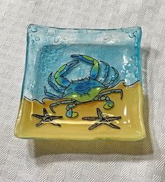 a blue and yellow plate with a crab on the beach in it's center