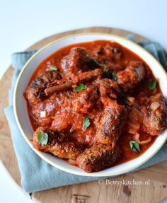 a white bowl filled with meat covered in sauce on top of a wooden cutting board