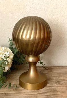 a gold vase sitting on top of a wooden table next to white and green flowers