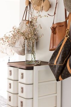 two purses hanging on the wall next to a vase with flowers