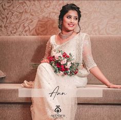 a woman sitting on a couch wearing a white sari and holding a bouquet of flowers