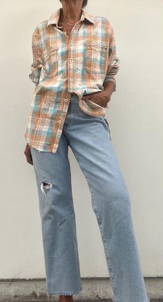 an older woman standing in front of a white wall wearing jeans and a plaid shirt