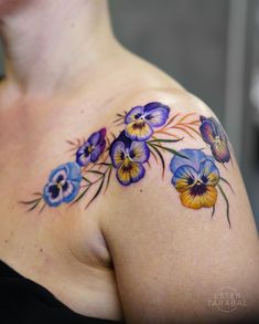 a woman's shoulder with blue and yellow flowers on her left arm, tattoo artist