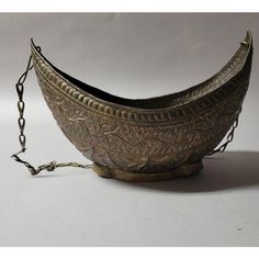 an old metal bowl with chains hanging from it's sides on a white surface