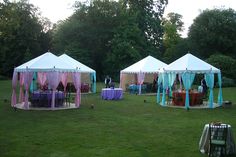 several tents set up in the middle of a grassy field with tables and chairs under them