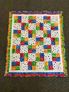 a multicolored quilt on the floor with polka dots and squares in it's center