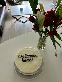 a welcome home cake sitting on a table with flowers in a vase next to it