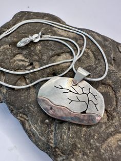 a necklace with a tree on it sitting on top of a rock next to a chain