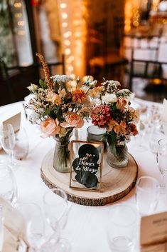 two vases filled with flowers sitting on top of a wooden table covered in wine glasses