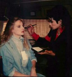 the woman is getting her make up done by the man in the blue suit and red shirt