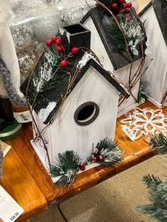 three birdhouses decorated with evergreen and red berries sit on a wooden table in front of other christmas decorations