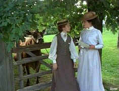 two women standing next to each other in front of a fence with cows behind them