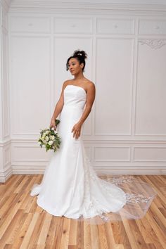 a woman in a white wedding dress standing on a hard wood floor holding a bouquet