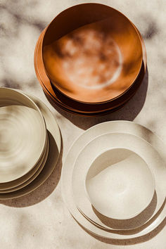 three plates and two bowls on a marble table top with shadows from the sun shining through them