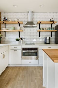 a kitchen with white cabinets and open shelving on the wall above the stove top