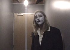 a woman with makeup painted on her face standing in front of a bathroom stall door