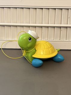 a small toy turtle with a white hat on its head sitting on the floor next to a wall