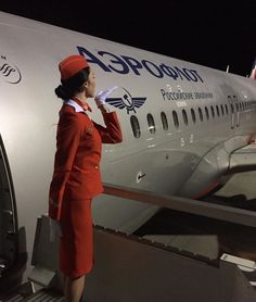 a woman in an orange suit is standing next to the door of a large airplane