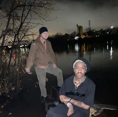 two men sitting next to each other in front of a body of water at night