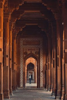 an archway in the middle of a building with columns and arches on both sides, leading to a person standing at the end