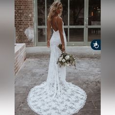 a woman in a white wedding dress holding a bouquet and looking at the camera with a brick building behind her