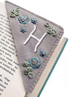 an open book with flowers on it next to a felt triangle that has the letter h