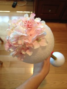 a person holding a white vase with pink flowers on it and a ball in the middle