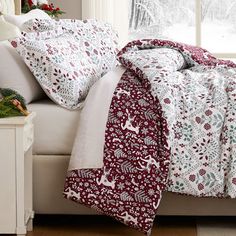 a bed covered in white and red sheets next to a window with christmas decorations on it