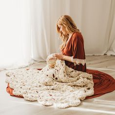 a woman is sitting on the floor with a crocheted blanket