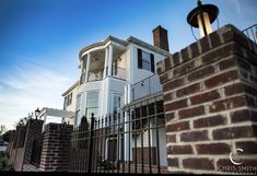 a large white house behind a fence with a light on it's post in the foreground