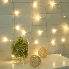 a white table topped with a vase filled with flowers next to a wall covered in fairy lights