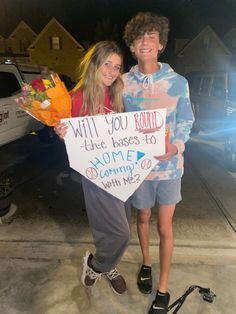 two people standing next to each other holding flowers and a sign that says will you round the bases to home coming soon?