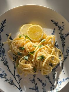 a white plate topped with pasta covered in lemon sauce and garnished with herbs