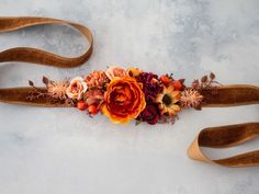 an orange and red flower arrangement on a brown ribbon tied to a white surface with other flowers