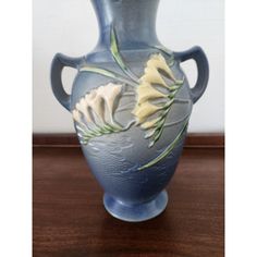 a blue vase sitting on top of a wooden table next to a white and yellow flower